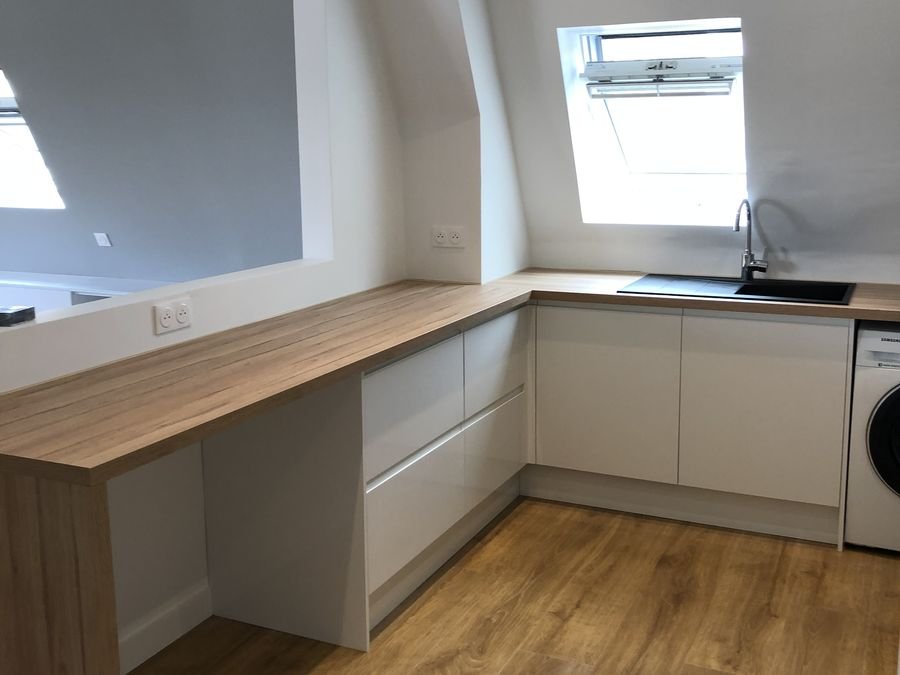 Cuisine sous combles avec plan de travail en bois, meubles blancs et fenêtre de toit