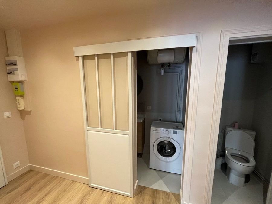 Buanderie avec lave-linge derrière une porte coulissante vitrée