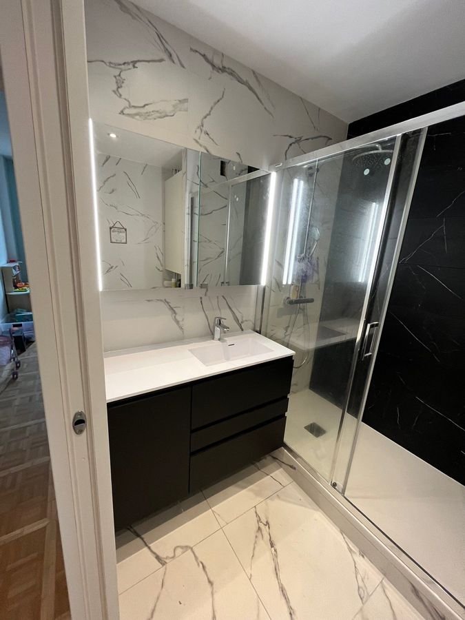 Salle de bains avec vasque suspendue, miroir lumineux et douche à l'italienne en marbre